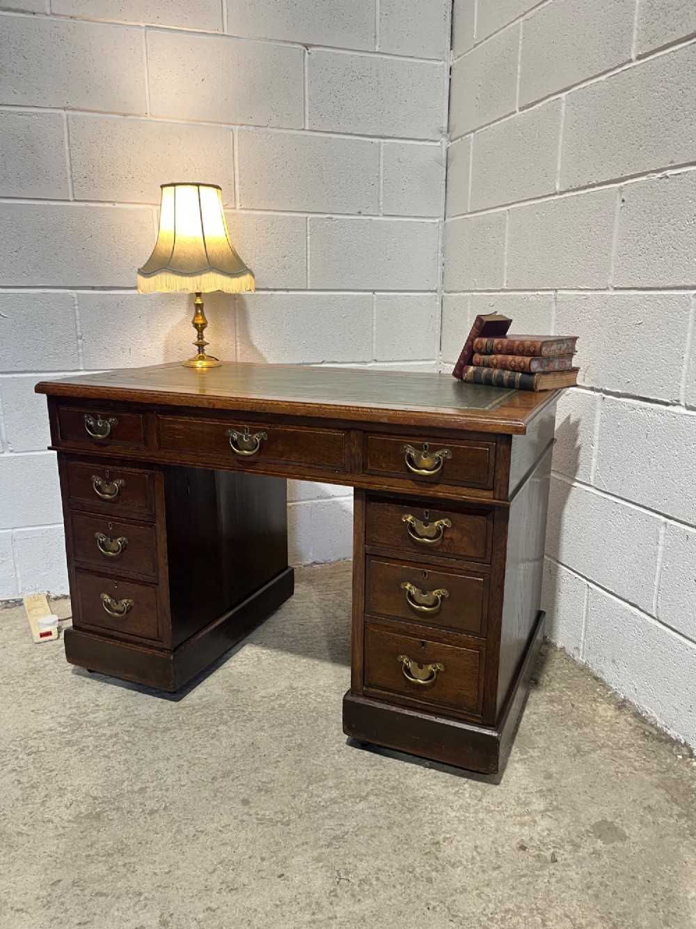 A late 19th-century dark oak freestanding pedestal desk featuring a green leather inset writing surface, nine drawers with brass handles, and plinth bases.