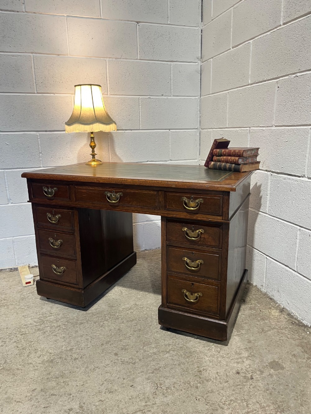 A late 19th-century dark oak freestanding pedestal desk featuring a green leather inset writing surface, nine drawers with brass handles, and plinth bases. View II