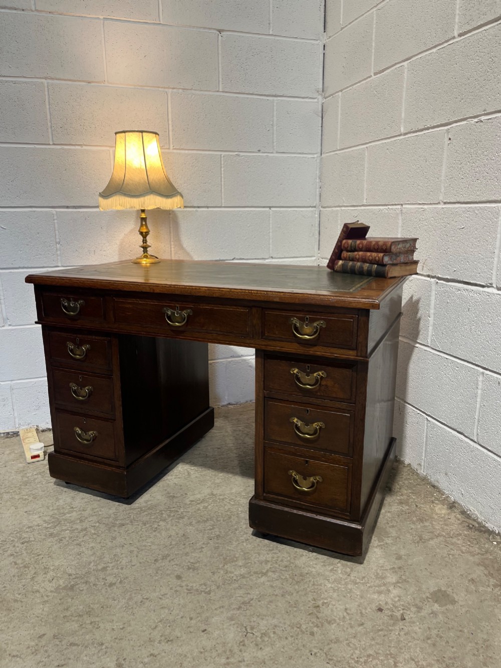 A late 19th-century dark oak freestanding pedestal desk featuring a green leather inset writing surface, nine drawers with brass handles, and plinth bases. View III