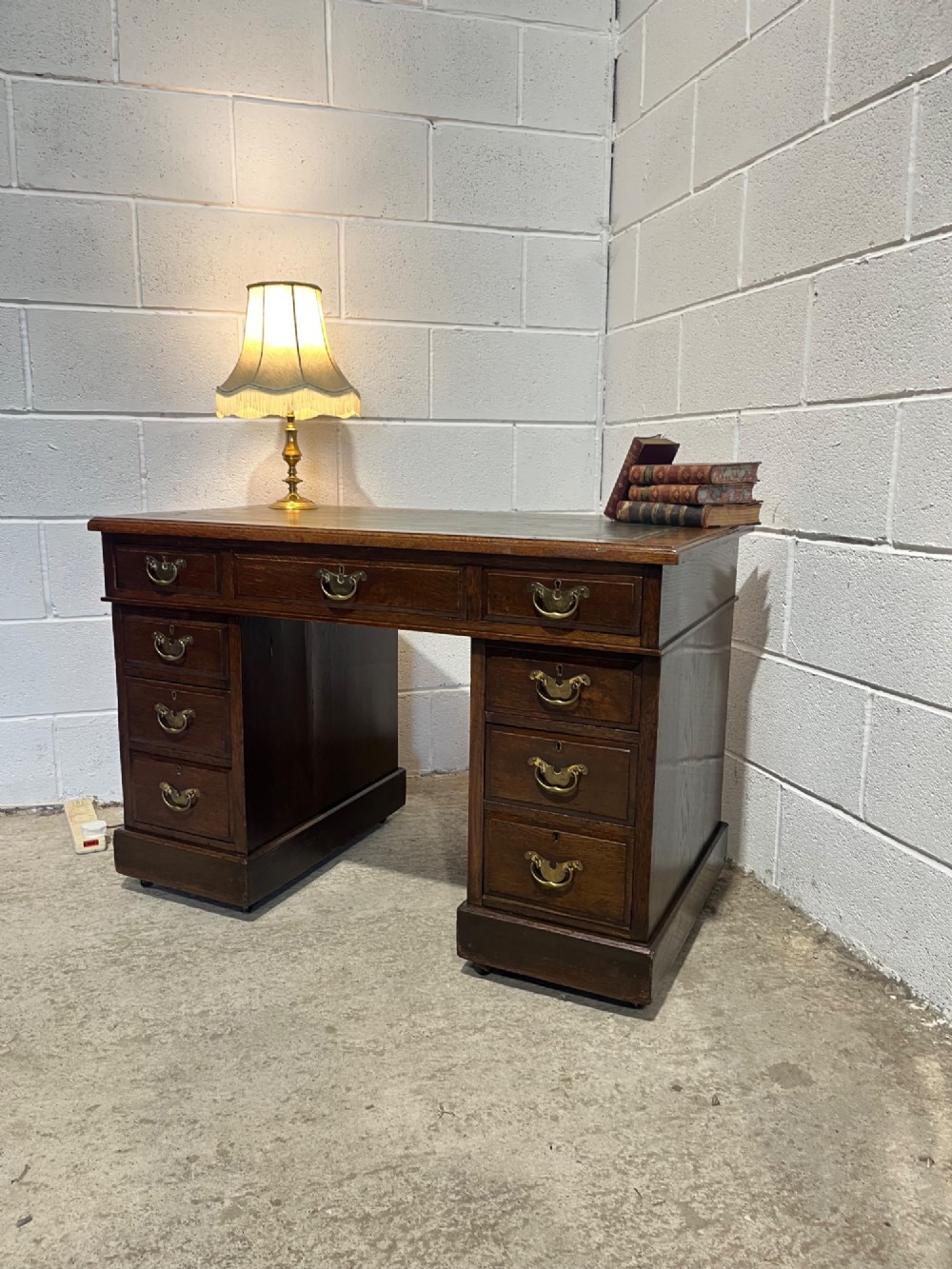 A late 19th-century dark oak freestanding pedestal desk featuring a green leather inset writing surface, nine drawers with brass handles, and plinth bases. View IV