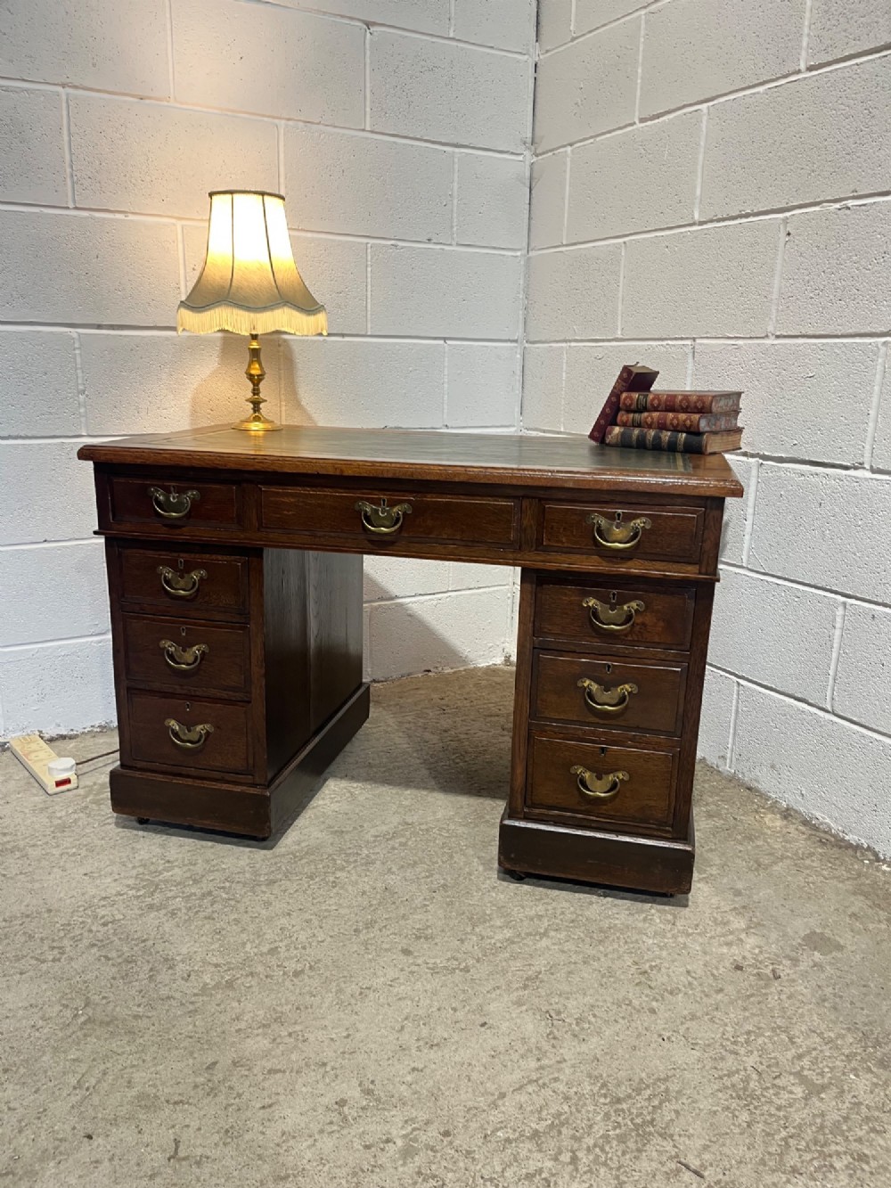 A late 19th-century dark oak freestanding pedestal desk featuring a green leather inset writing surface, nine drawers with brass handles, and plinth bases. View V
