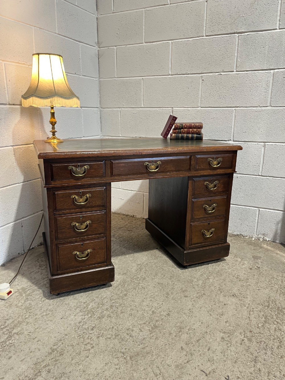 A late 19th-century dark oak freestanding pedestal desk featuring a green leather inset writing surface, nine drawers with brass handles, and plinth bases. View VI