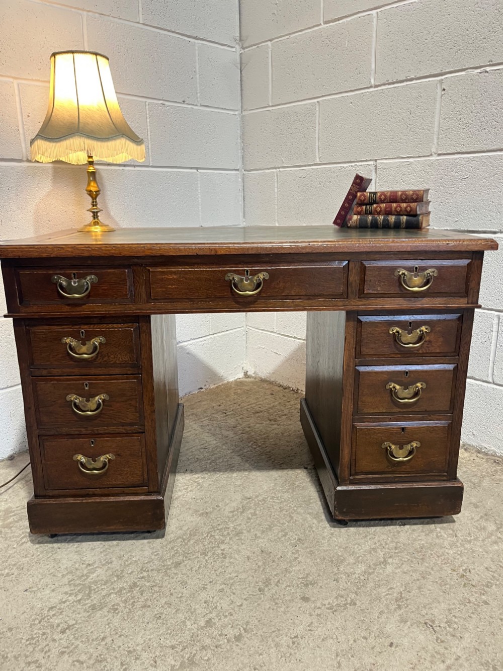 A late 19th-century dark oak freestanding pedestal desk featuring a green leather inset writing surface, nine drawers with brass handles, and plinth bases. View VII