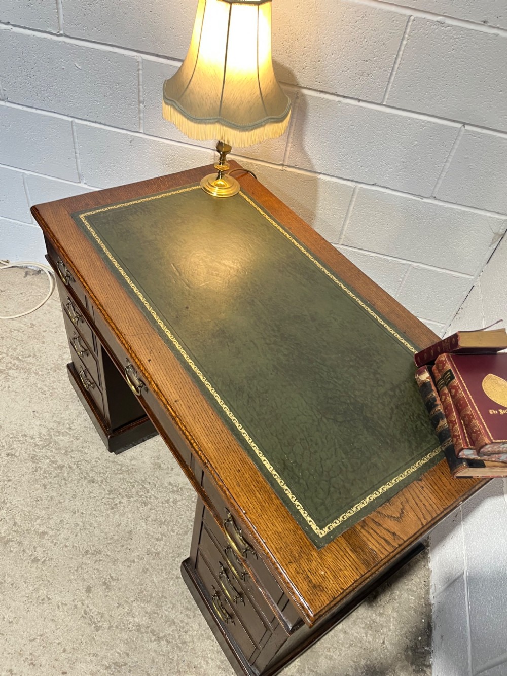 A late 19th-century dark oak freestanding pedestal desk featuring a green leather inset writing surface, nine drawers with brass handles, and plinth bases. View VIII