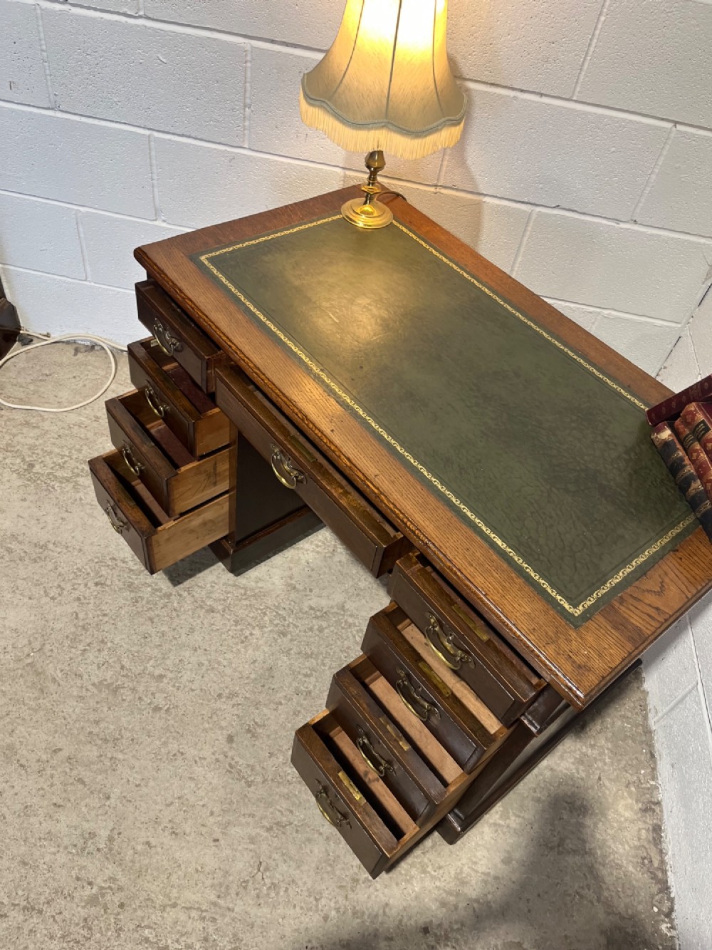 A late 19th-century dark oak freestanding pedestal desk featuring a green leather inset writing surface, nine drawers with brass handles, and plinth bases. View X