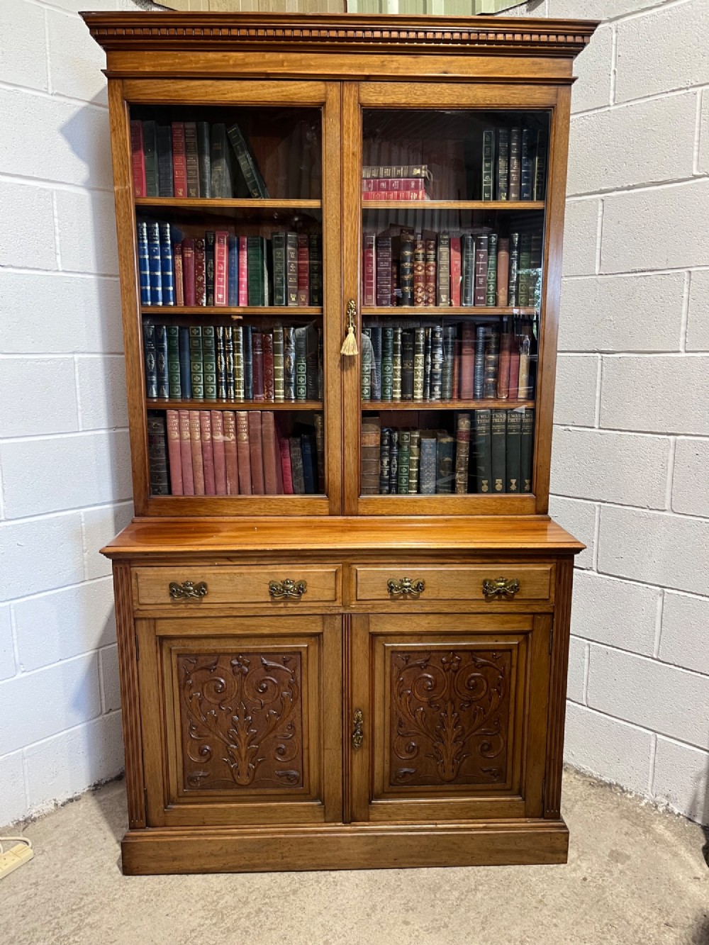 A 19th-century mahogany glazed bookcase featuring upper double glass doors filled with books, middle drawers, and lower doors with carved foliate panels.