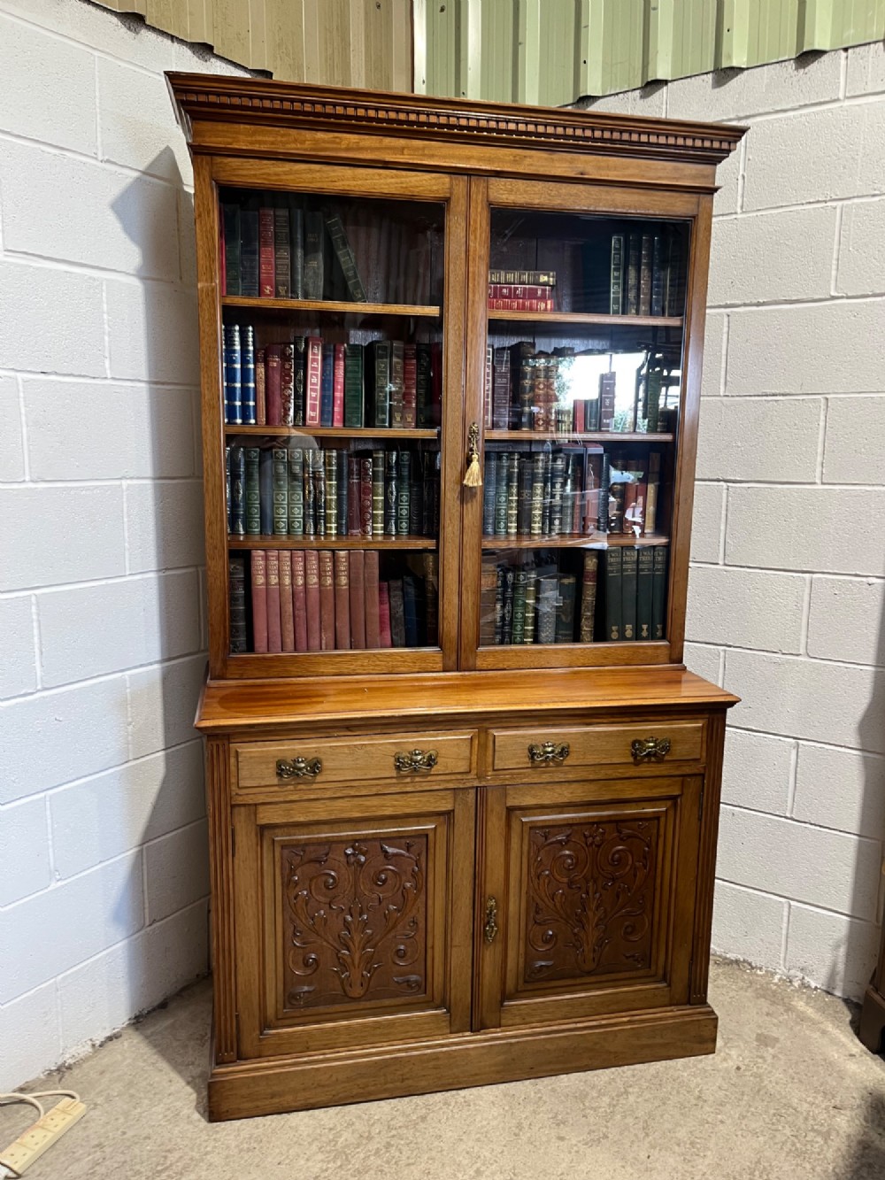 A 19th-century mahogany glazed bookcase featuring upper double glass doors filled with books, middle drawers, and lower doors with carved foliate panels. View III