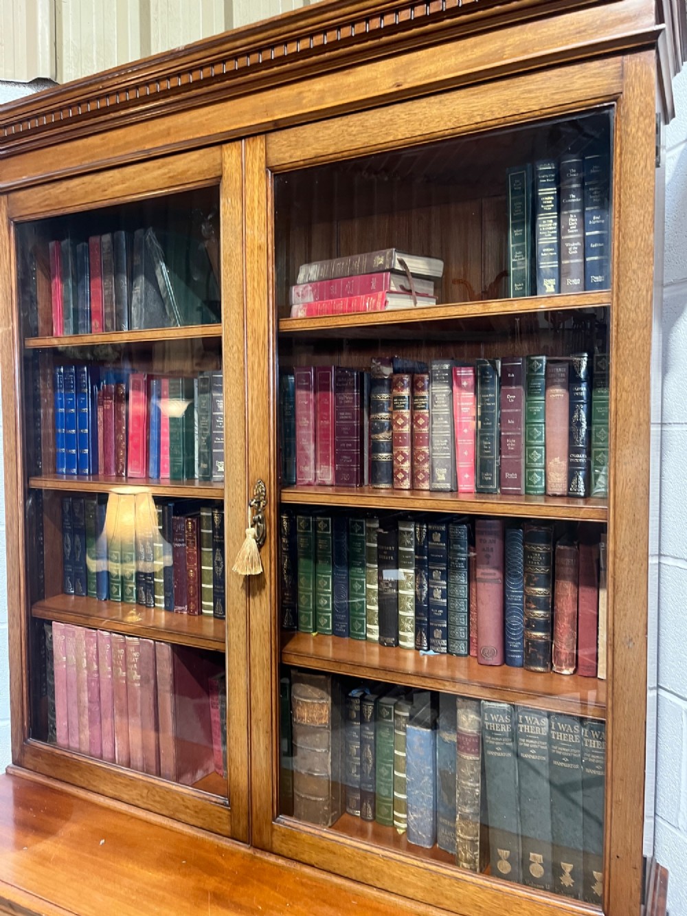 A 19th-century mahogany glazed bookcase featuring upper double glass doors filled with books, middle drawers, and lower doors with carved foliate panels. View IV