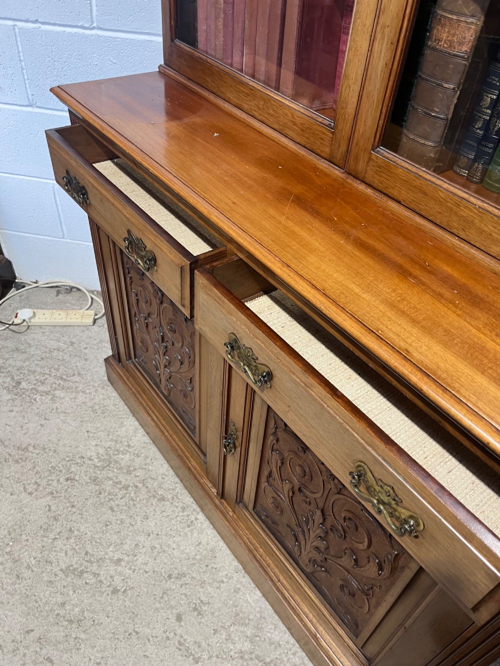 A 19th-century mahogany glazed bookcase featuring upper double glass doors filled with books, middle drawers, and lower doors with carved foliate panels. View IX