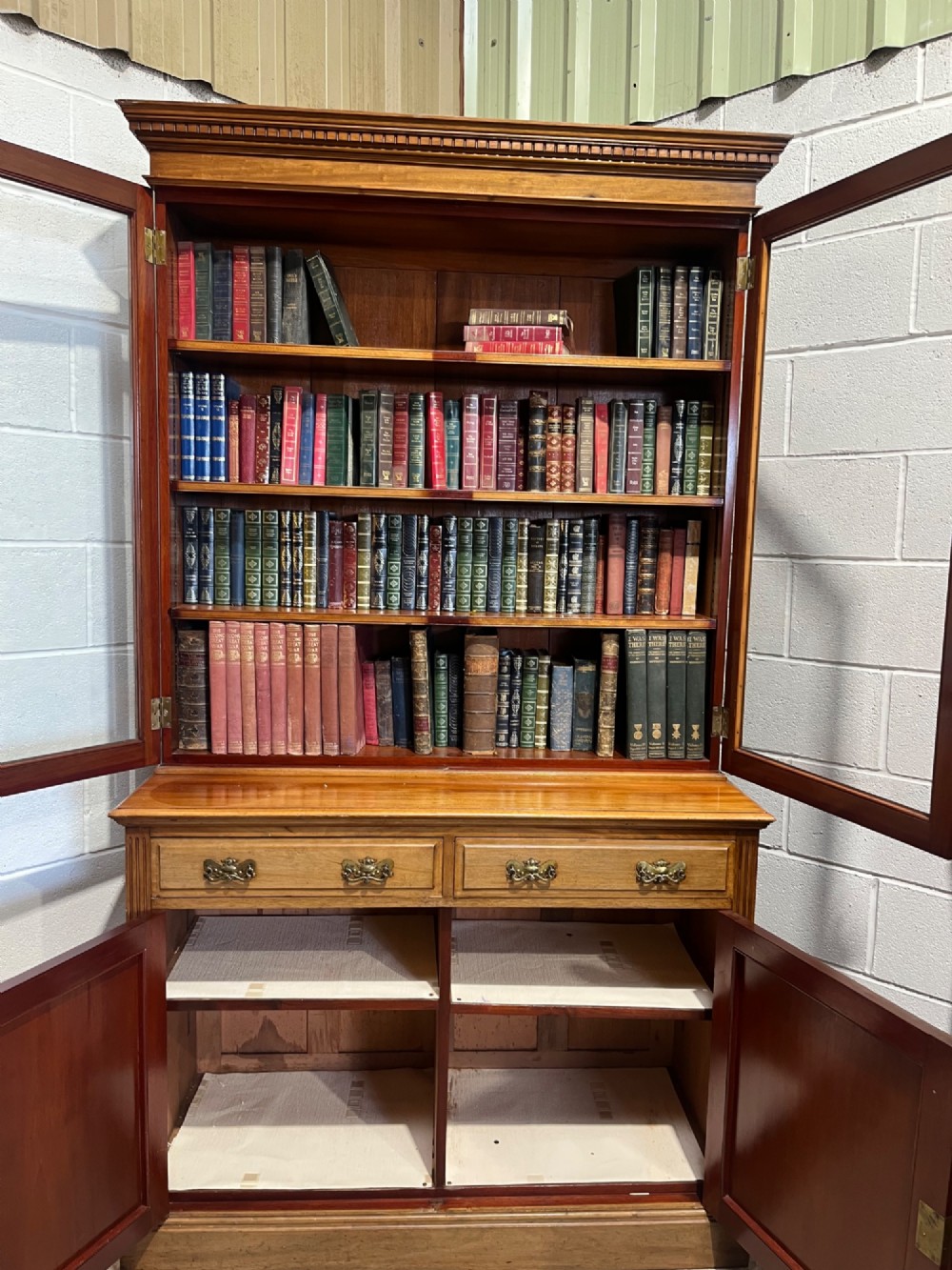 A 19th-century mahogany glazed bookcase featuring upper double glass doors filled with books, middle drawers, and lower doors with carved foliate panels. View XIII
