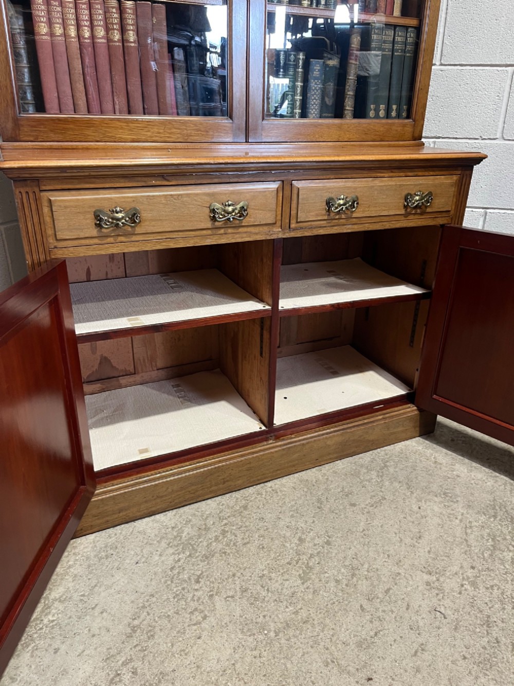 A 19th-century mahogany glazed bookcase featuring upper double glass doors filled with books, middle drawers, and lower doors with carved foliate panels. View XIV