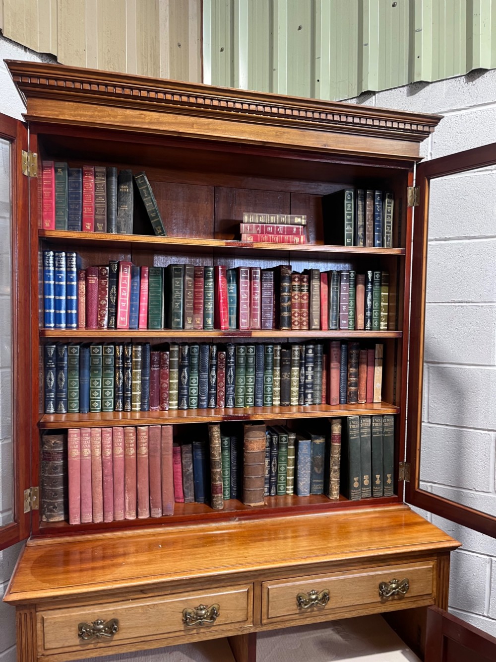 A 19th-century mahogany glazed bookcase featuring upper double glass doors filled with books, middle drawers, and lower doors with carved foliate panels. View XV