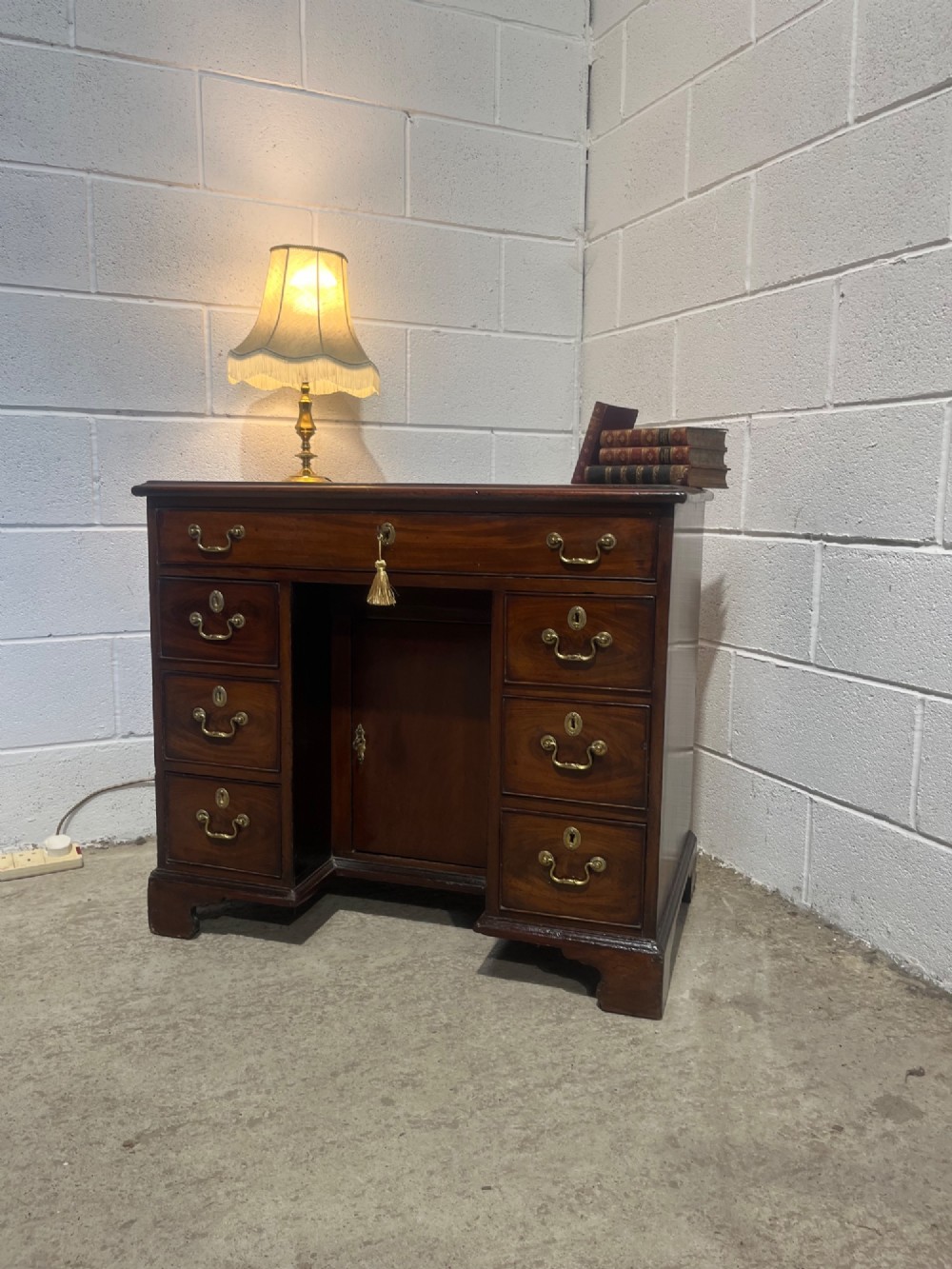 A George III mahogany kneehole desk with a full-width upper drawer over six side drawers, a central recessed cupboard, brass swan-neck handles, and bracket feet. View II