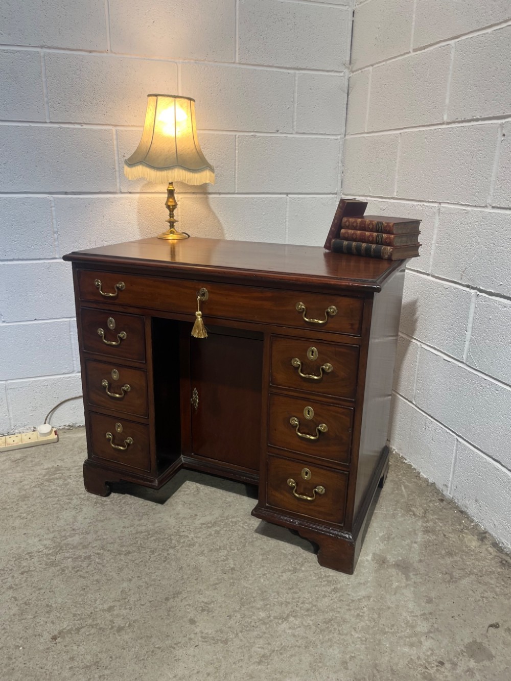 A George III mahogany kneehole desk with a full-width upper drawer over six side drawers, a central recessed cupboard, brass swan-neck handles, and bracket feet. View III
