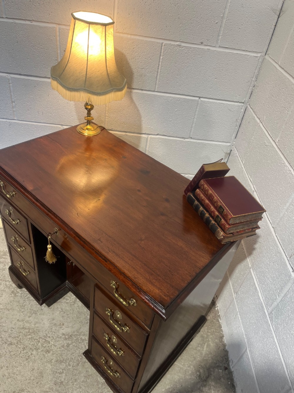 A George III mahogany kneehole desk with a full-width upper drawer over six side drawers, a central recessed cupboard, brass swan-neck handles, and bracket feet. View IV