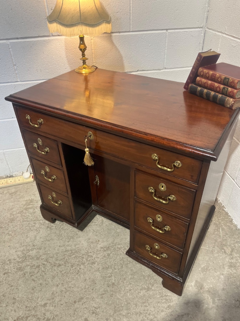A George III mahogany kneehole desk with a full-width upper drawer over six side drawers, a central recessed cupboard, brass swan-neck handles, and bracket feet. View V