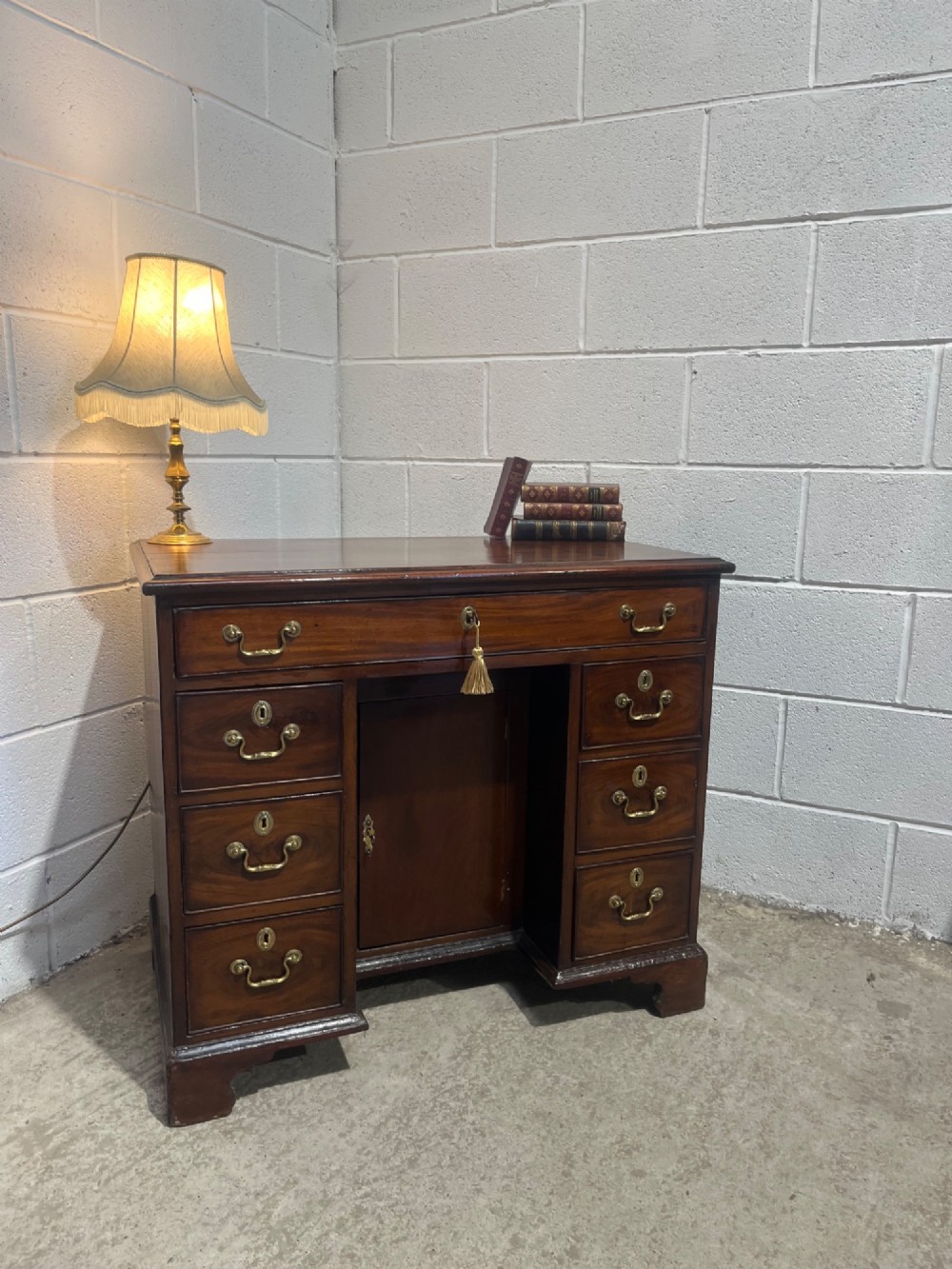 A George III mahogany kneehole desk with a full-width upper drawer over six side drawers, a central recessed cupboard, brass swan-neck handles, and bracket feet. View VI