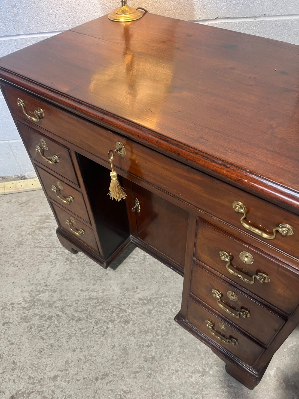 A George III mahogany kneehole desk with a full-width upper drawer over six side drawers, a central recessed cupboard, brass swan-neck handles, and bracket feet. View VIII