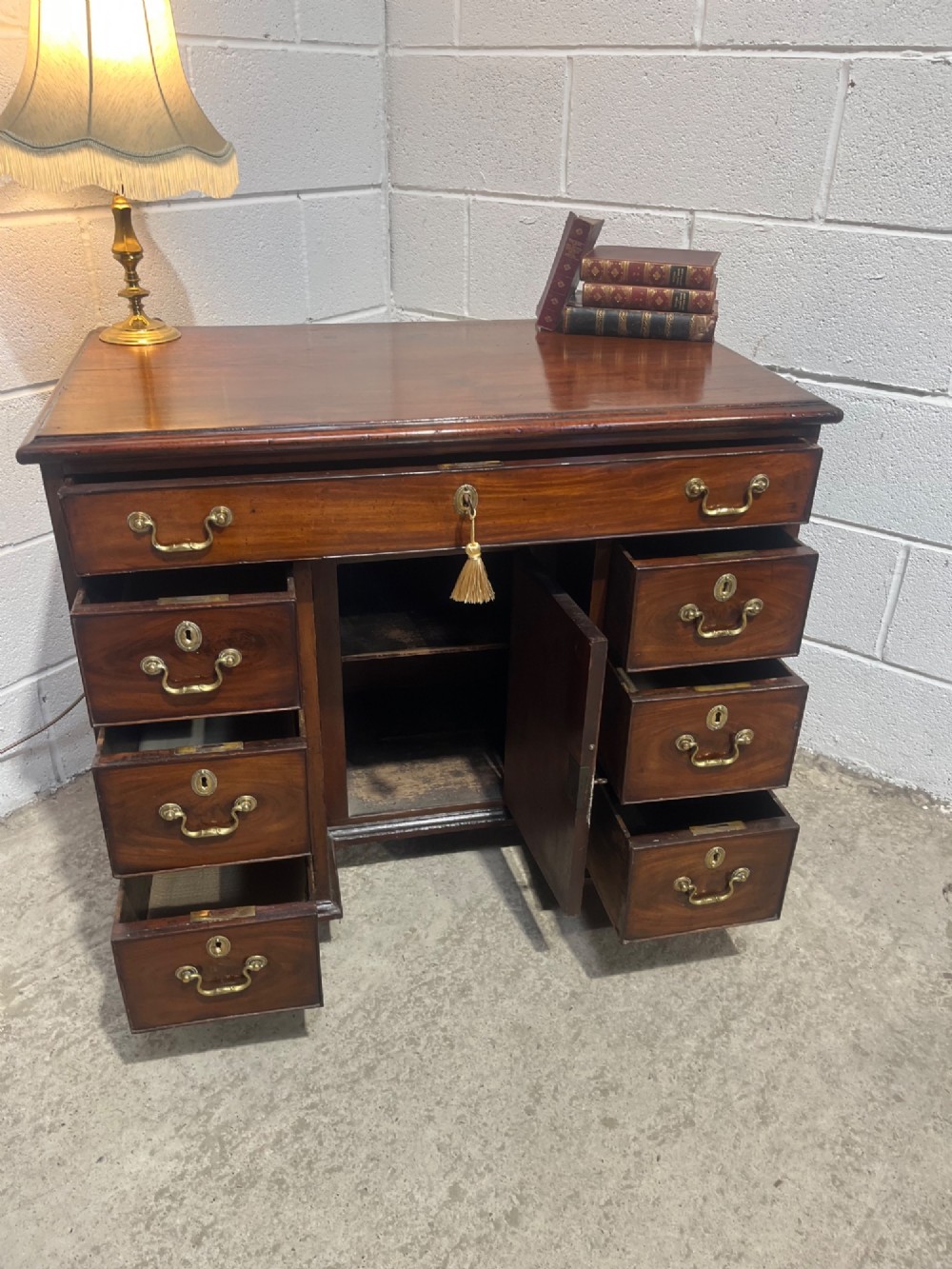 A George III mahogany kneehole desk with a full-width upper drawer over six side drawers, a central recessed cupboard, brass swan-neck handles, and bracket feet. View XI