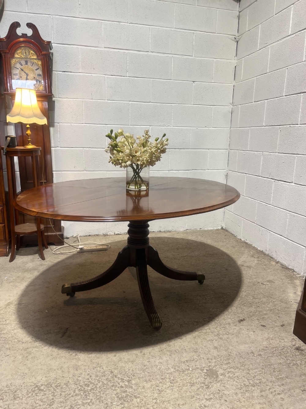 A circular antique Regency mahogany dining table featuring a central turned column and four reeded splayed legs with brass castors.