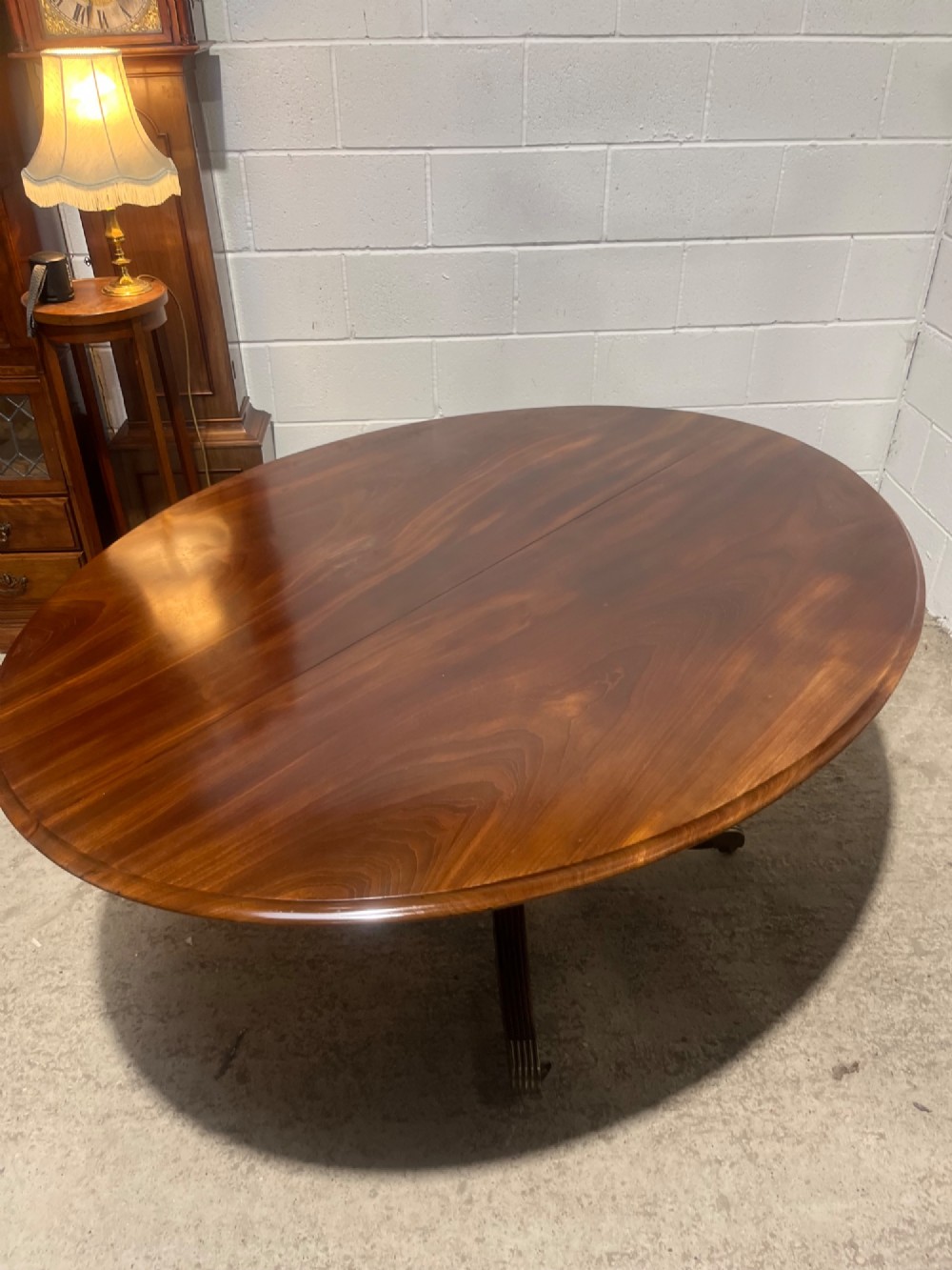 A circular antique Regency mahogany dining table featuring a central turned column and four reeded splayed legs with brass castors. View III