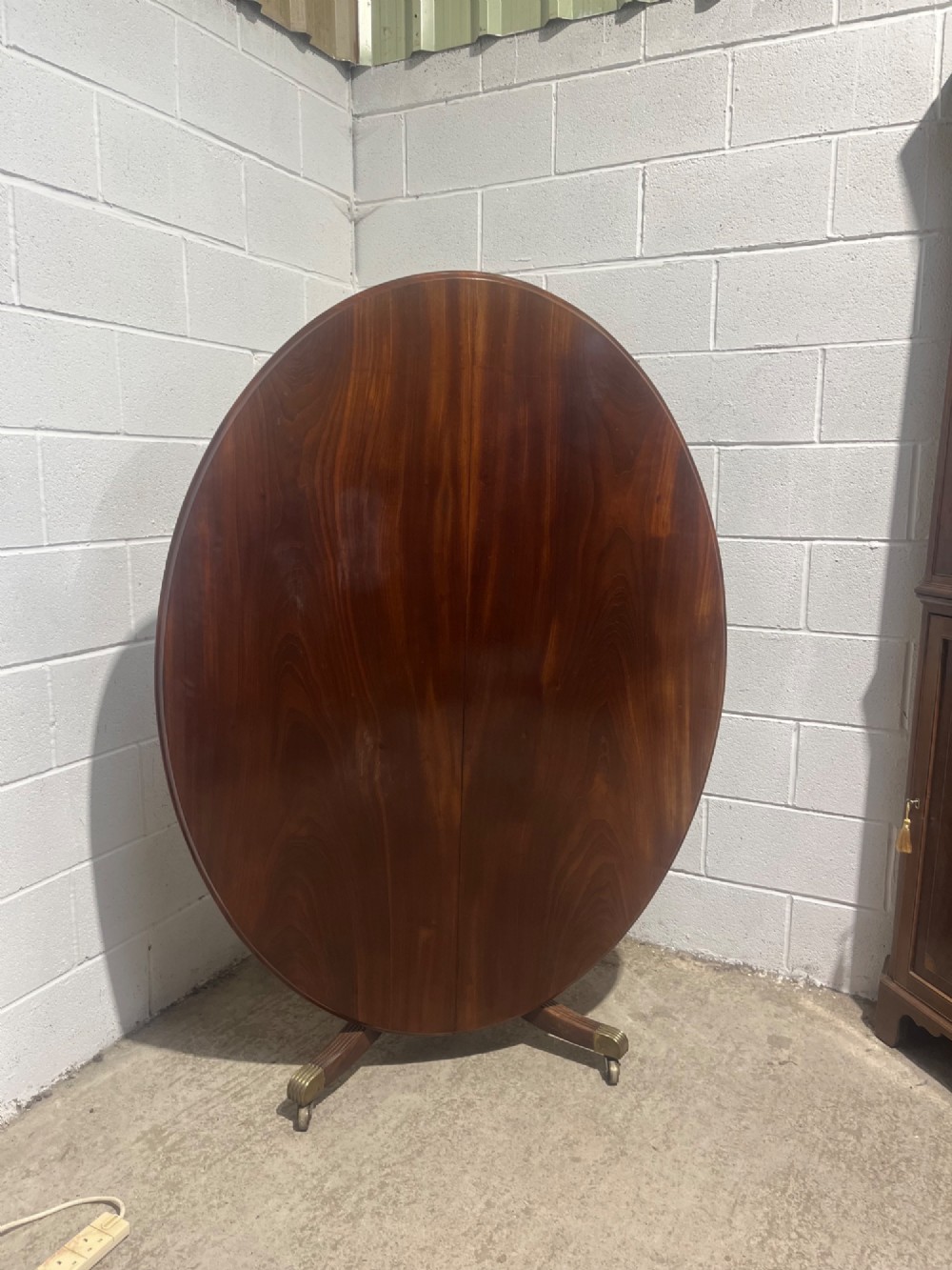 A circular antique Regency mahogany dining table featuring a central turned column and four reeded splayed legs with brass castors. View VIII