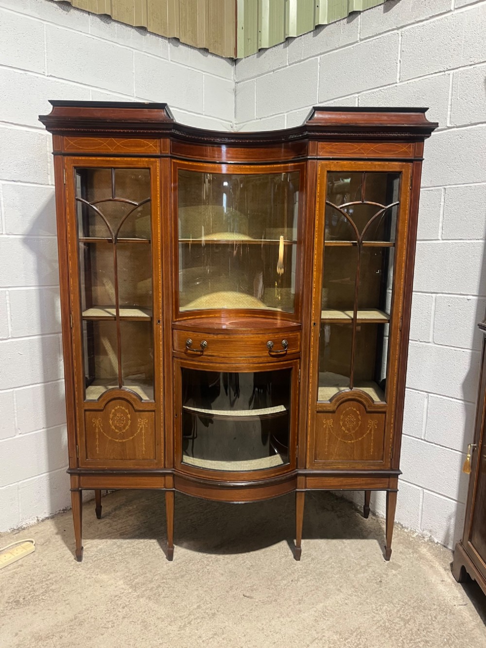 An antique inlaid mahogany display cabinet featuring a concave glazed central section, satinwood marquetry swags, astragal glazing bars, and tapered square legs. View III