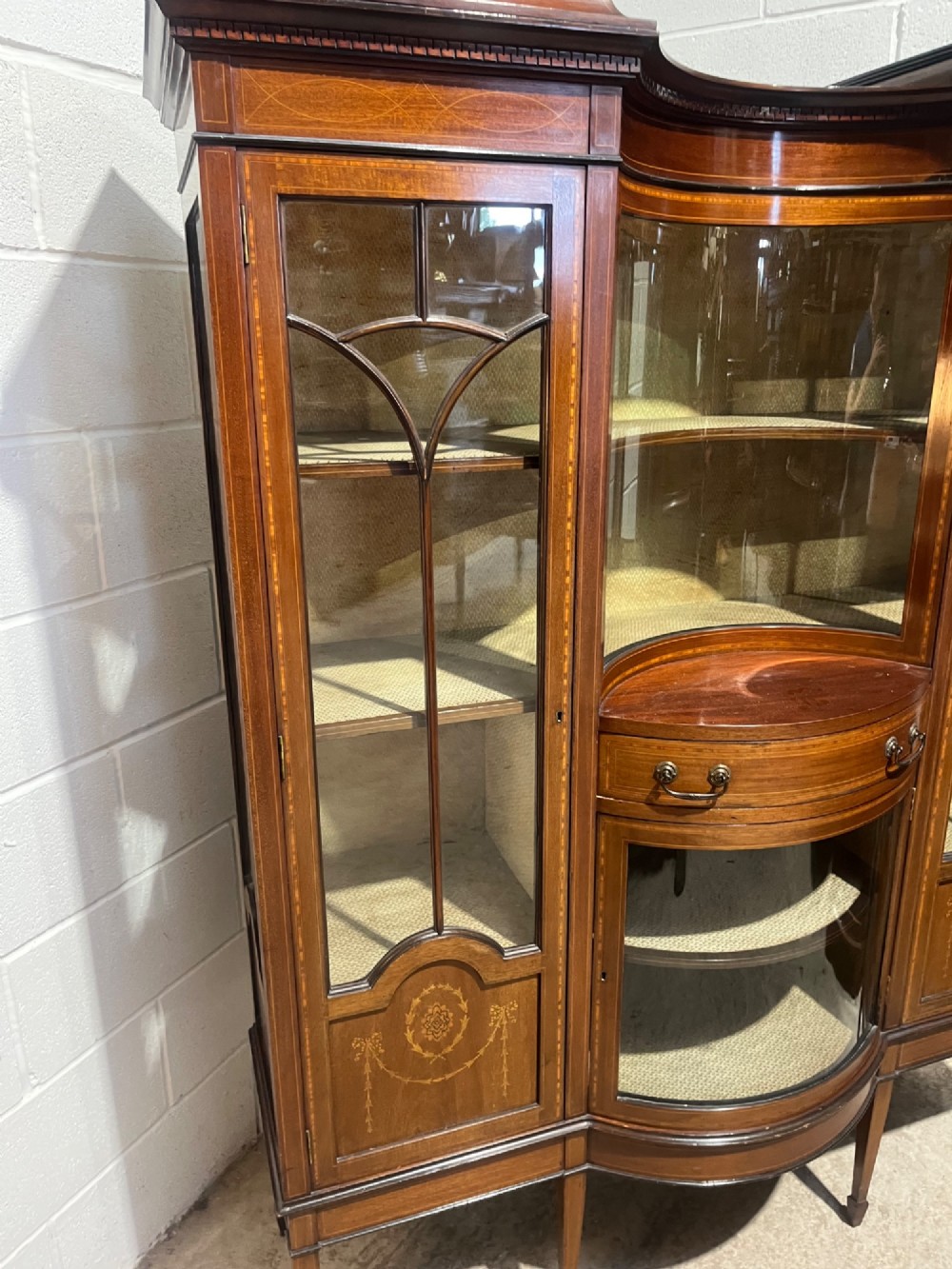 An antique inlaid mahogany display cabinet featuring a concave glazed central section, satinwood marquetry swags, astragal glazing bars, and tapered square legs. View VII