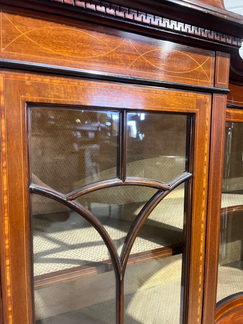 An antique inlaid mahogany display cabinet featuring a concave glazed central section, satinwood marquetry swags, astragal glazing bars, and tapered square legs. View VIII