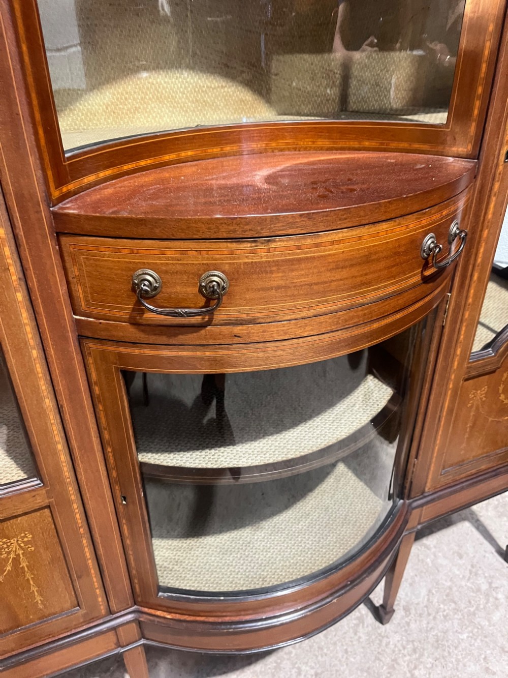 An antique inlaid mahogany display cabinet featuring a concave glazed central section, satinwood marquetry swags, astragal glazing bars, and tapered square legs. View X