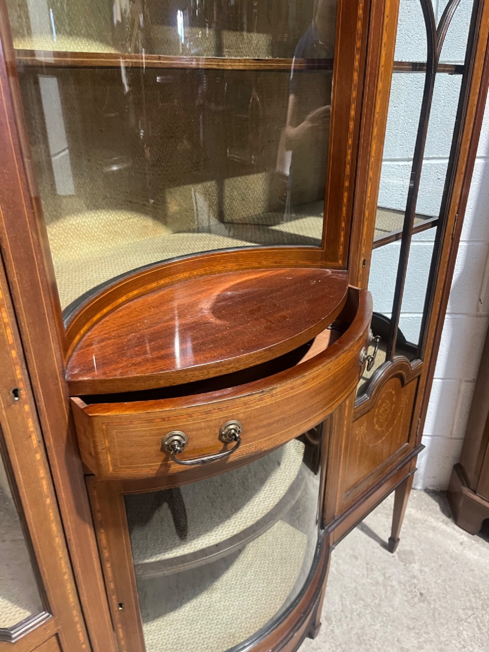 An antique inlaid mahogany display cabinet featuring a concave glazed central section, satinwood marquetry swags, astragal glazing bars, and tapered square legs. View XI