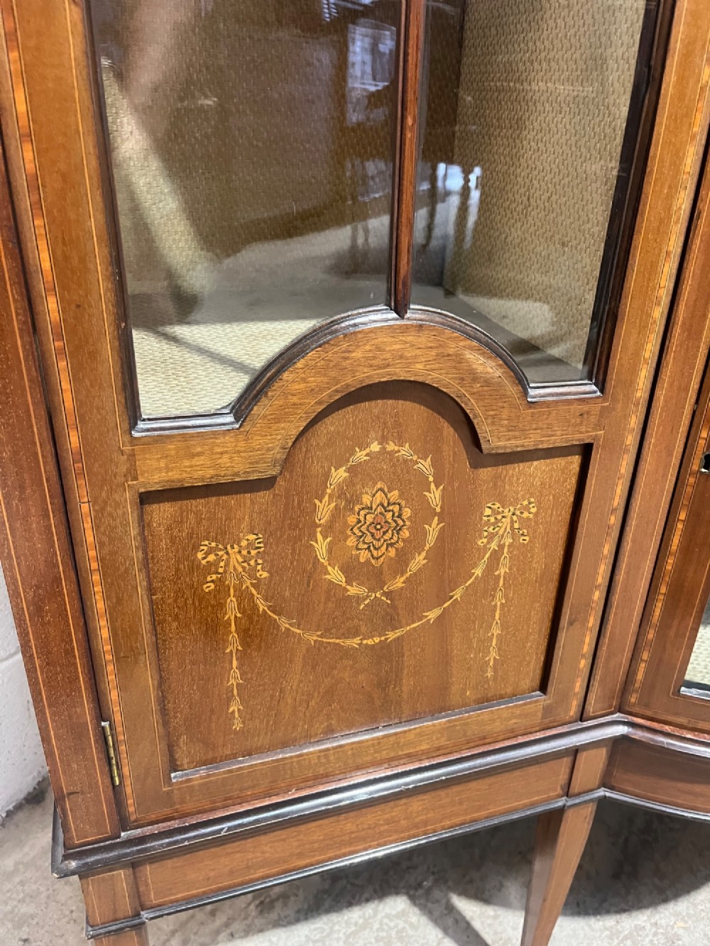 An antique inlaid mahogany display cabinet featuring a concave glazed central section, satinwood marquetry swags, astragal glazing bars, and tapered square legs. View XII