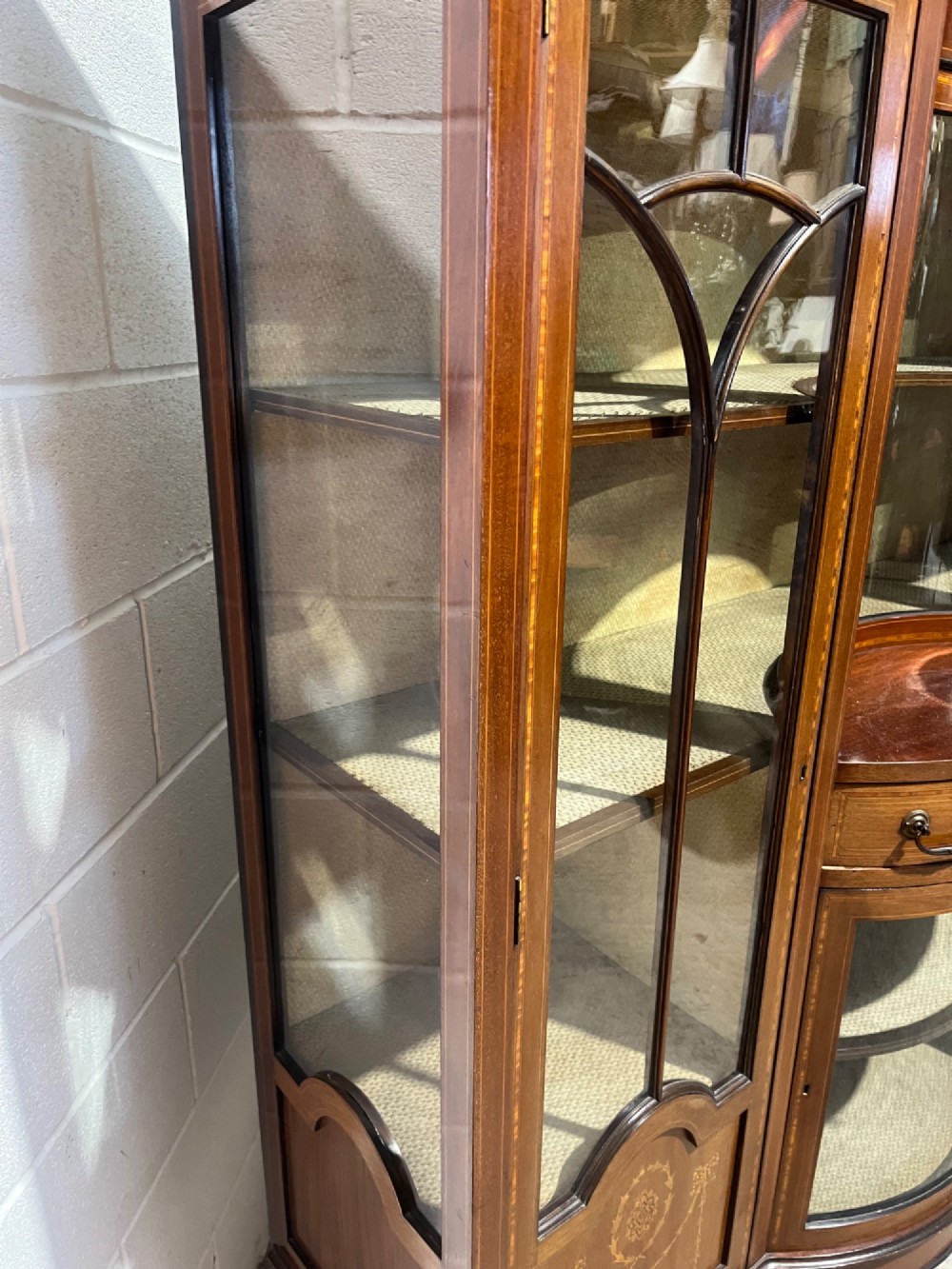 An antique inlaid mahogany display cabinet featuring a concave glazed central section, satinwood marquetry swags, astragal glazing bars, and tapered square legs. View XIII