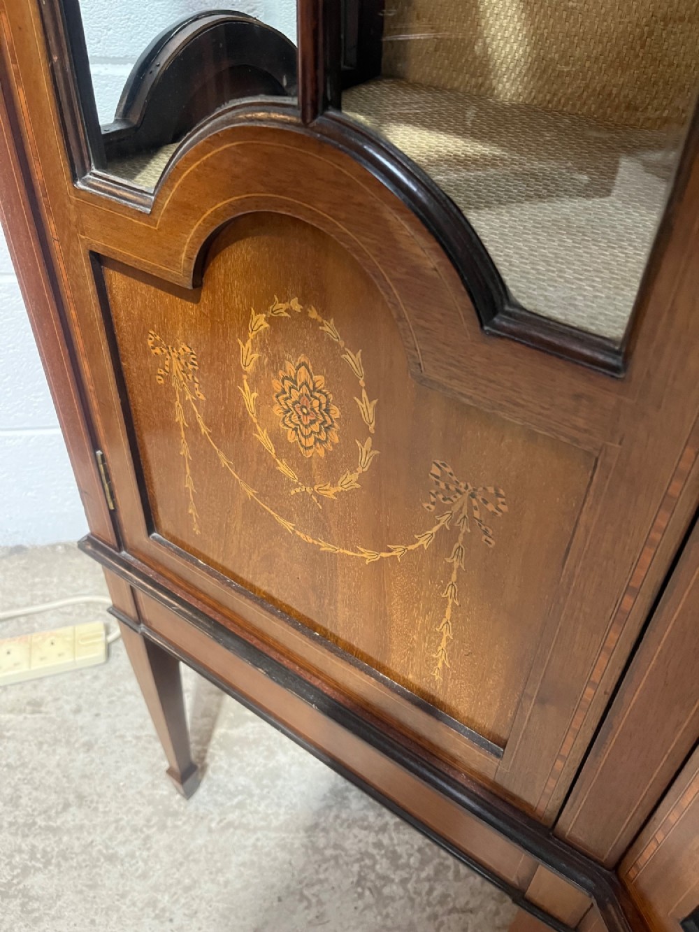 An antique inlaid mahogany display cabinet featuring a concave glazed central section, satinwood marquetry swags, astragal glazing bars, and tapered square legs. View XV