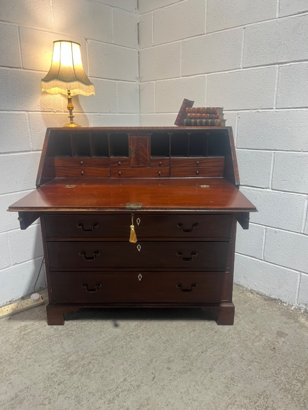 A Georgian mahogany writing bureau with an open sloped lid revealing internal fitted pigeonholes and small drawers above three wide drawers with brass handles. View II