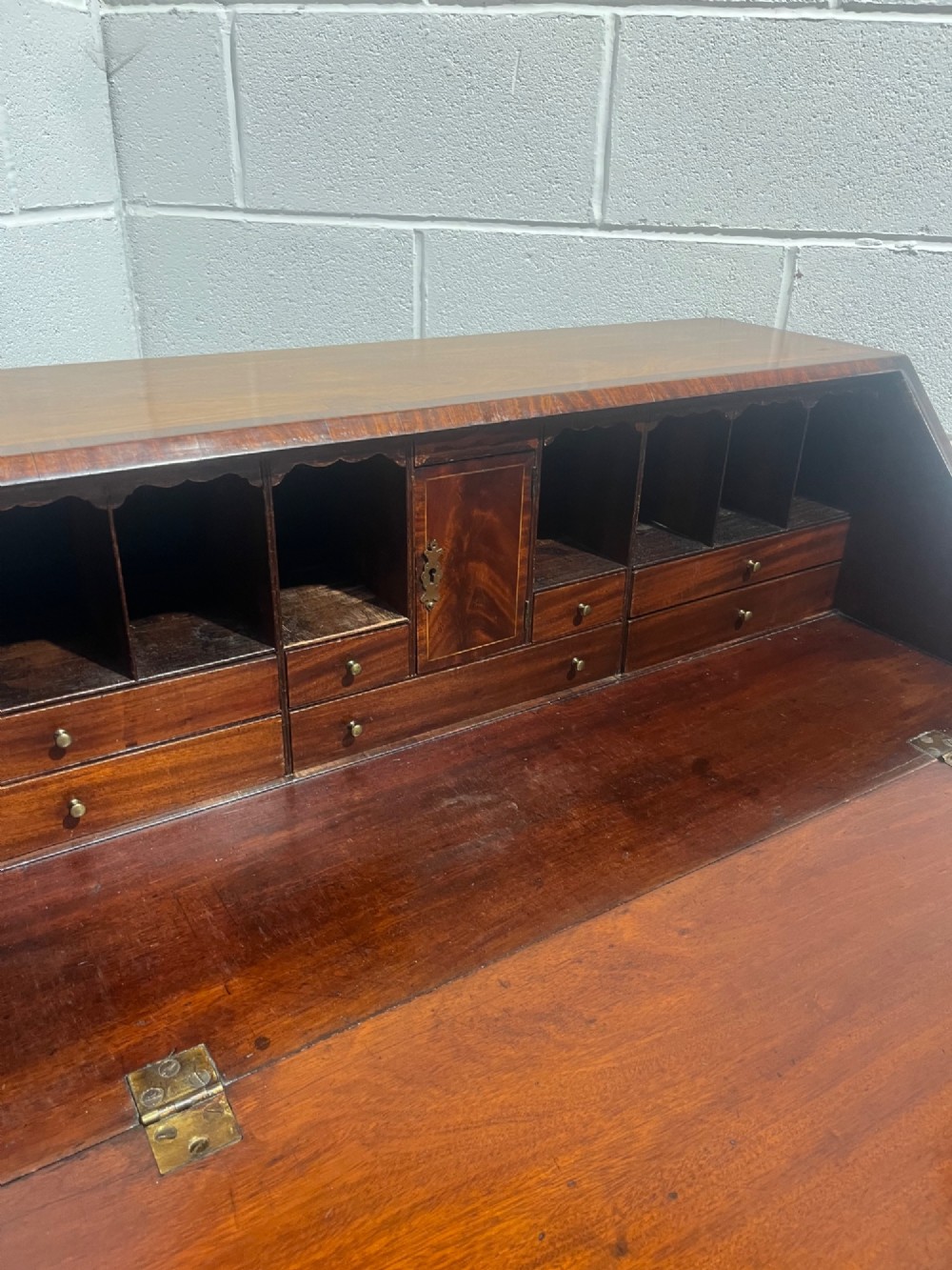 A Georgian mahogany writing bureau with an open sloped lid revealing internal fitted pigeonholes and small drawers above three wide drawers with brass handles. View V