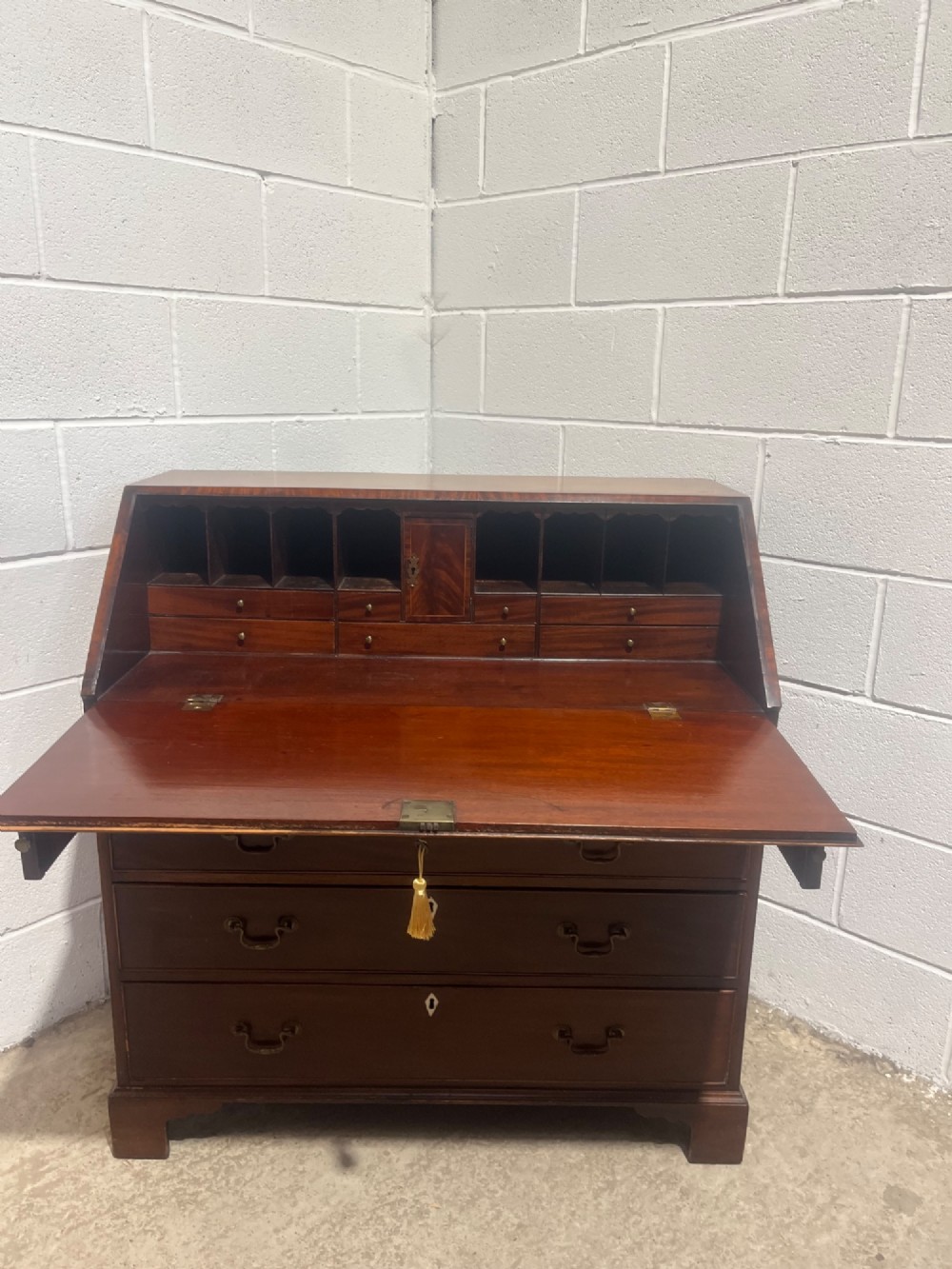 A Georgian mahogany writing bureau with an open sloped lid revealing internal fitted pigeonholes and small drawers above three wide drawers with brass handles. View VI