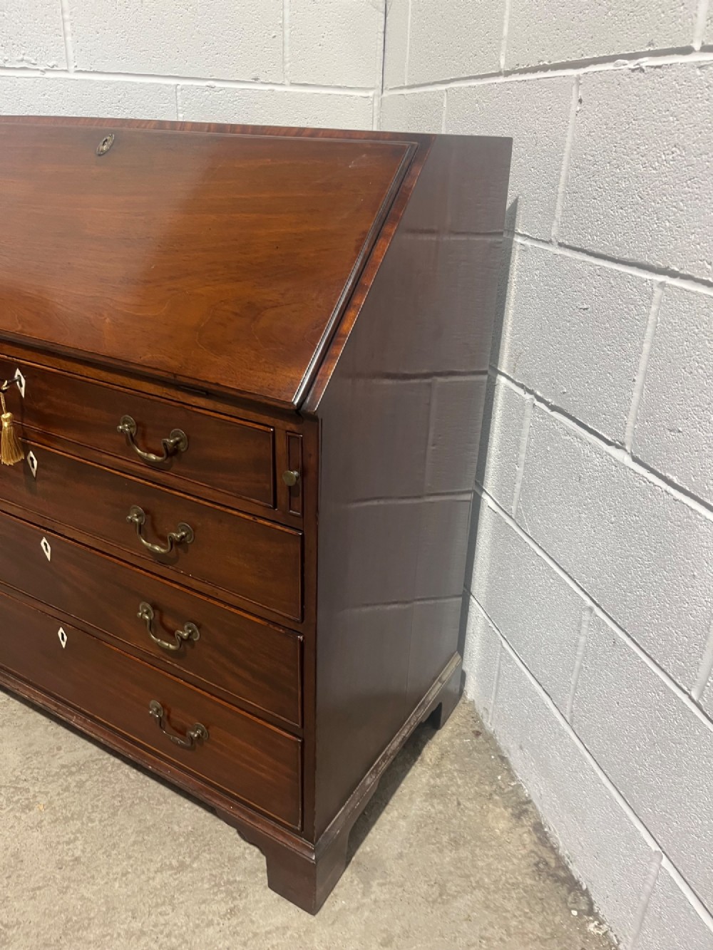 A Georgian mahogany writing bureau with an open sloped lid revealing internal fitted pigeonholes and small drawers above three wide drawers with brass handles. View IX