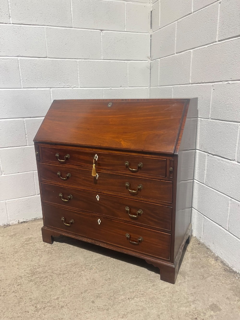 A Georgian mahogany writing bureau with an open sloped lid revealing internal fitted pigeonholes and small drawers above three wide drawers with brass handles. View X