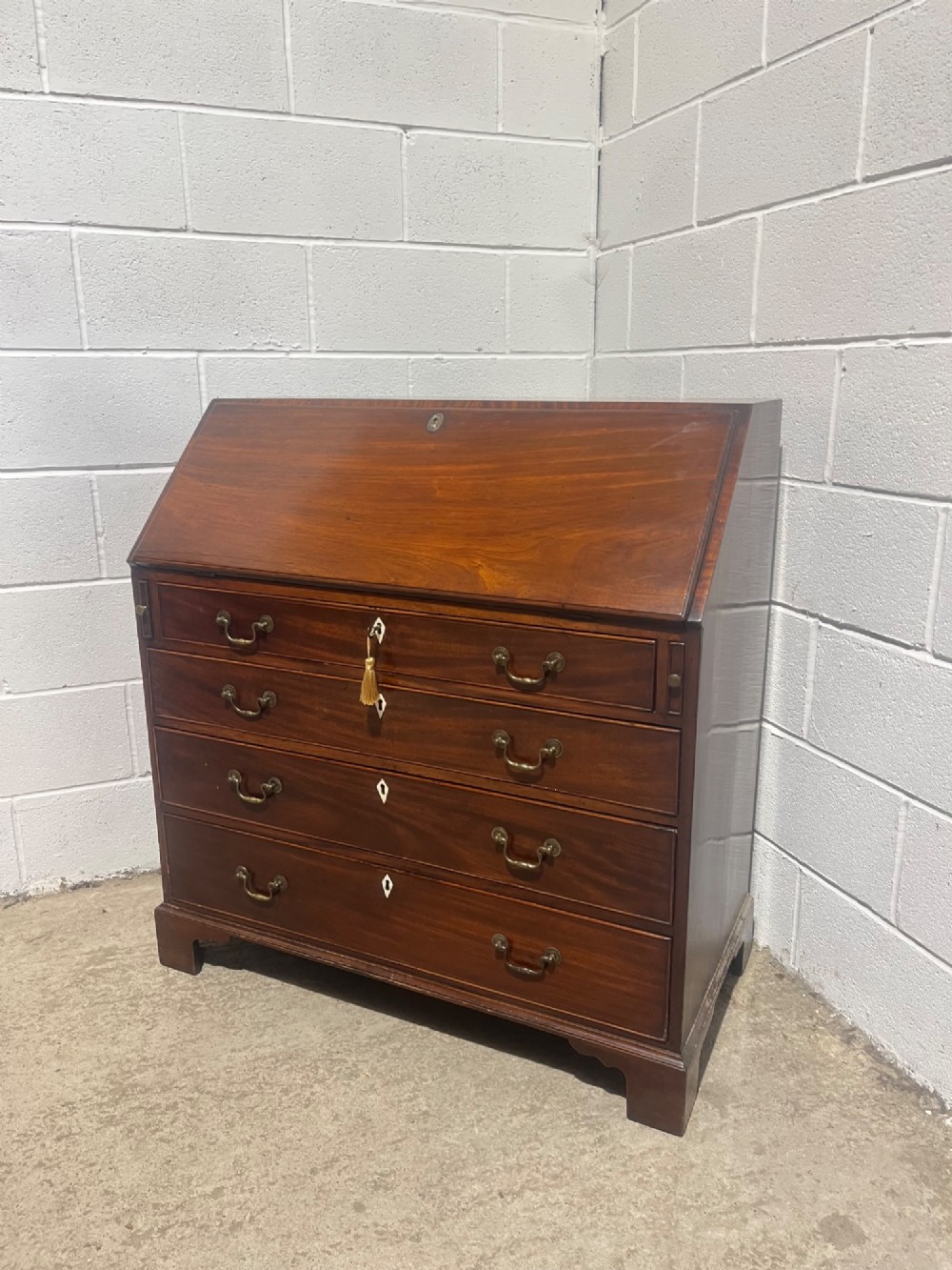A Georgian mahogany writing bureau with an open sloped lid revealing internal fitted pigeonholes and small drawers above three wide drawers with brass handles. View XI
