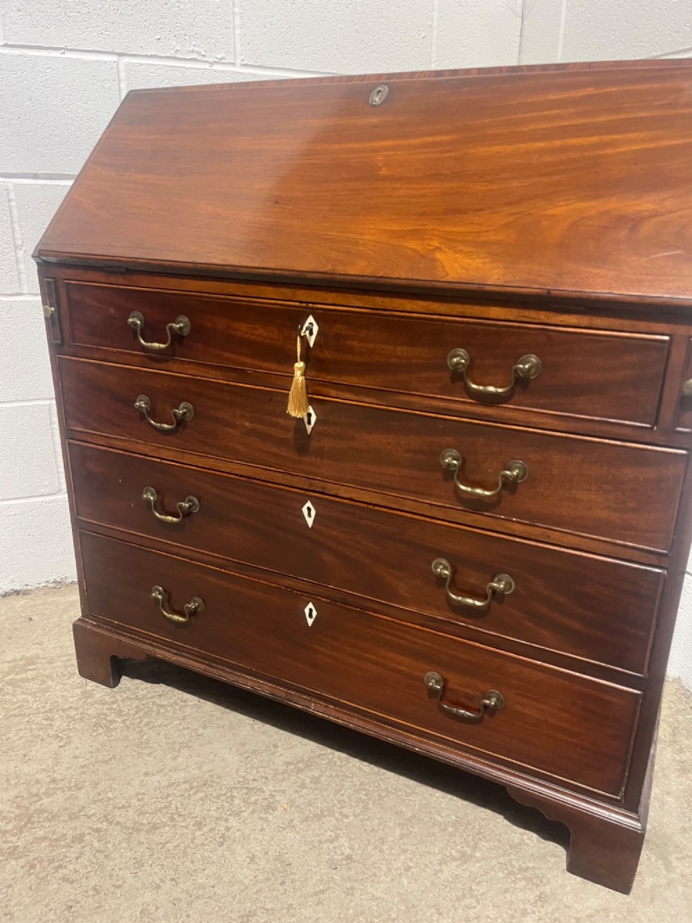 A Georgian mahogany writing bureau with an open sloped lid revealing internal fitted pigeonholes and small drawers above three wide drawers with brass handles. View XII