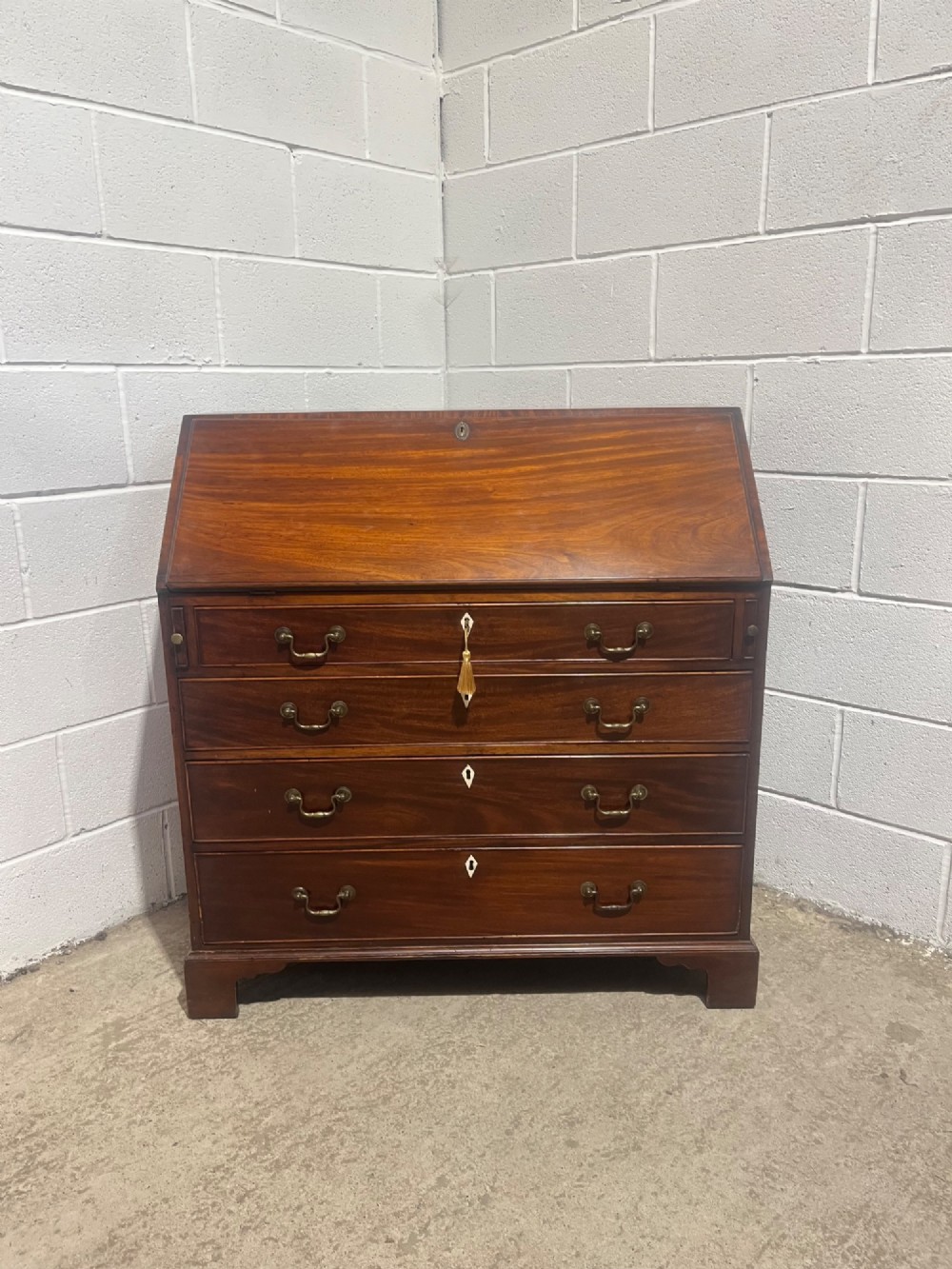 A Georgian mahogany writing bureau with an open sloped lid revealing internal fitted pigeonholes and small drawers above three wide drawers with brass handles. View XIII