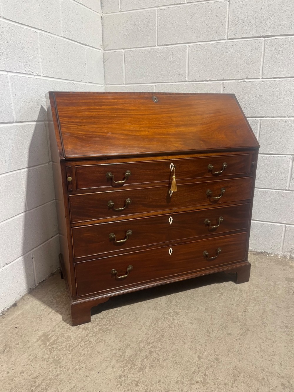 A Georgian mahogany writing bureau with an open sloped lid revealing internal fitted pigeonholes and small drawers above three wide drawers with brass handles. View XIV