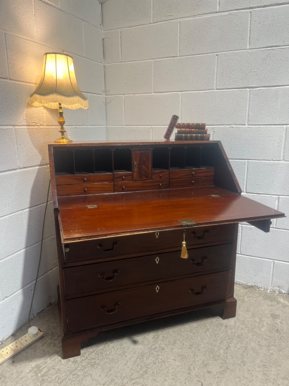 A Georgian mahogany writing bureau with an open sloped lid revealing internal fitted pigeonholes and small drawers above three wide drawers with brass handles. View XV