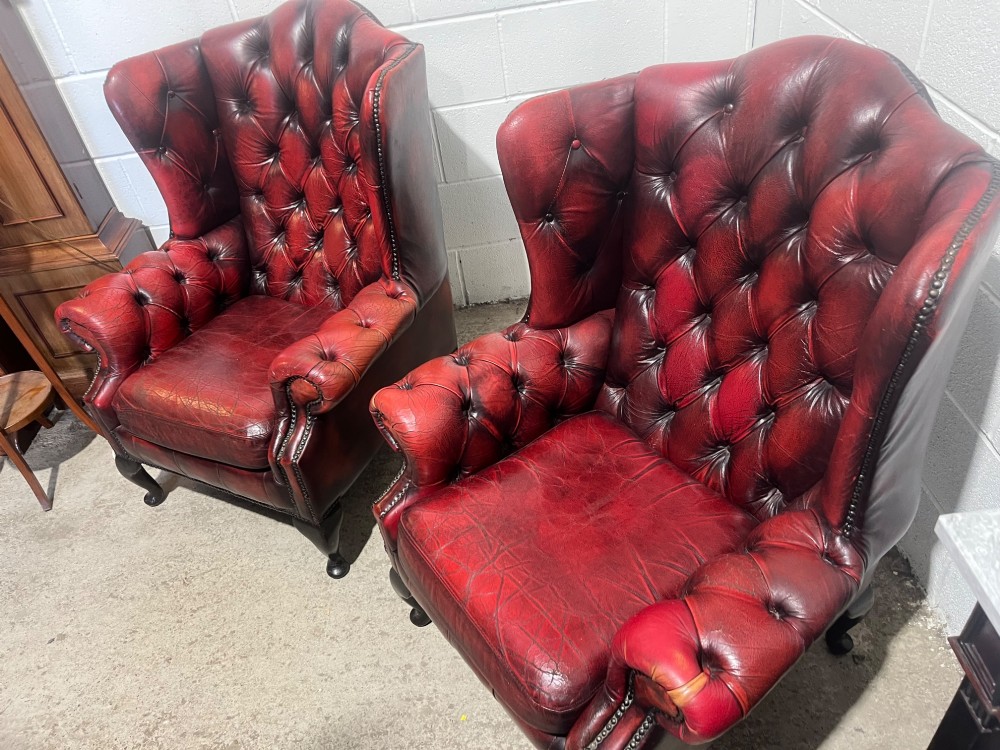 A pair of antique oxblood red leather Chesterfield wingback armchairs featuring deep button tufting, brass studding, and dark wooden cabriole front legs. View IV