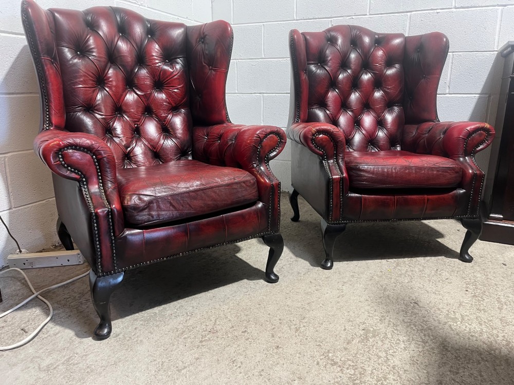 A pair of antique oxblood red leather Chesterfield wingback armchairs featuring deep button tufting, brass studding, and dark wooden cabriole front legs. View VIII