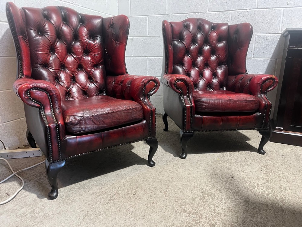 A pair of antique oxblood red leather Chesterfield wingback armchairs featuring deep button tufting, brass studding, and dark wooden cabriole front legs. View IX