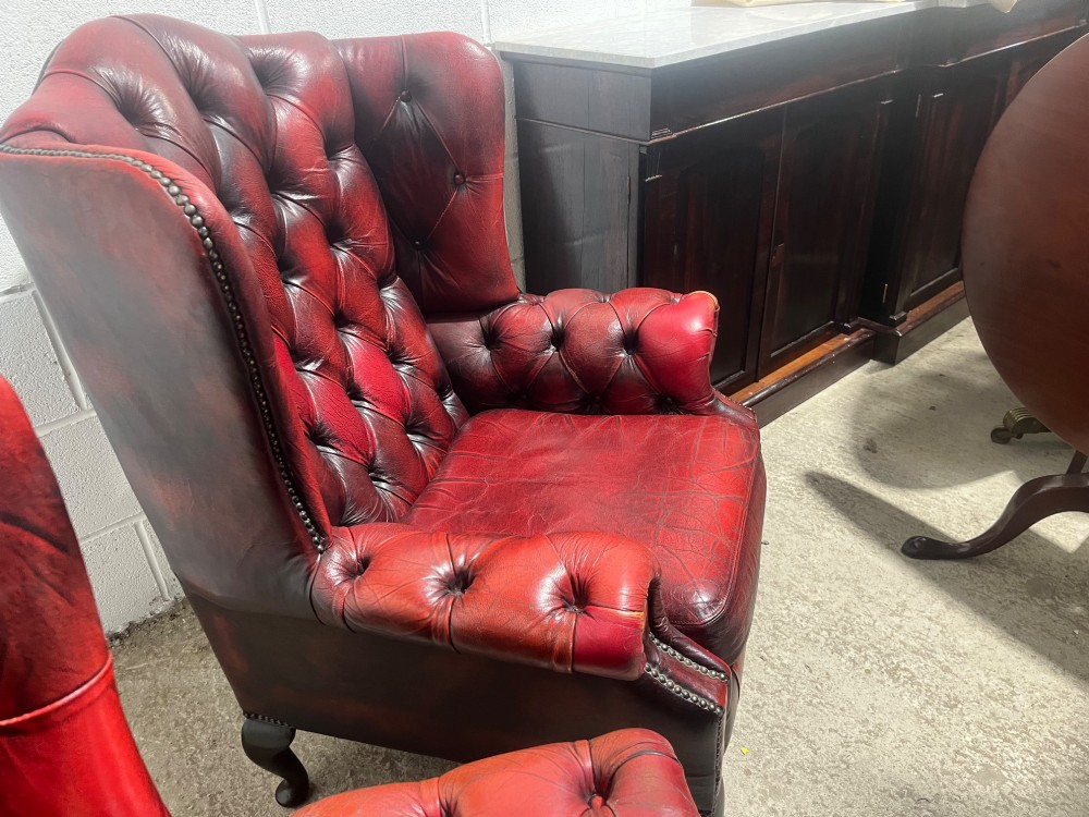 A pair of antique oxblood red leather Chesterfield wingback armchairs featuring deep button tufting, brass studding, and dark wooden cabriole front legs. View XII