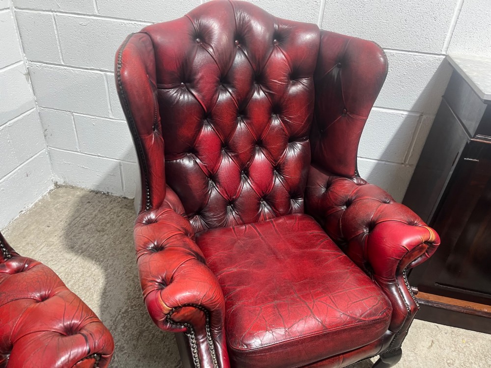 A pair of antique oxblood red leather Chesterfield wingback armchairs featuring deep button tufting, brass studding, and dark wooden cabriole front legs. View XIII