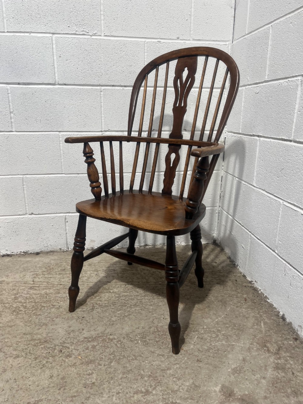 An antique 19th-century ash and elm high-back Windsor armchair featuring a hoop back with central pierced splat, turned arm supports, shaped saddle seat, and turned legs with an H-stretcher. View V